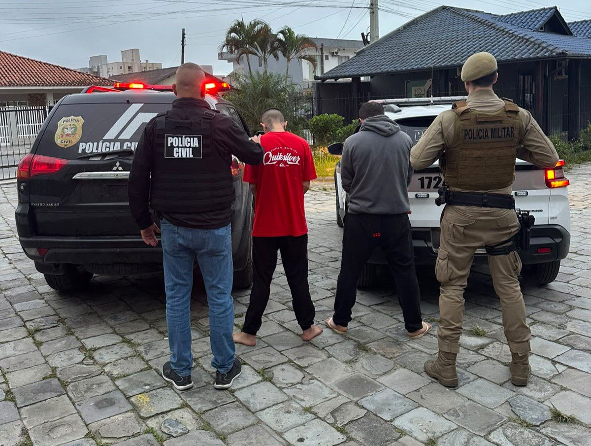 Operação conjunta das polícias Civil e Militar prende mandante de duplo homicídio e apreende armas e drogas Ação realizada na manhã desta quinta-feira (8) cumpriu mandado de prisão de suspeito de mandar matar casal no bairro Nossa Senhora das Graças, em Navegantes. Um segundo homem foi preso em flagrante no Distrito dos Kaetés, em Camboriú. Na manhã desta quinta-feira (8), uma operação conjunta entre a Polícia Civil (Delegacia de Navegantes) e a Polícia Militar (Agência de Inteligência e Tático do 25º BPM, com apoio do Tático do 12º BPM) cumpriu o mandado de prisão do mandante do duplo homicídio que vitimou Felipe Silva Santos e Fernanda Xisto Furtado. Durante as diligências, as equipes também cumpriram um mandado de busca e apreensão em um imóvel rural situado no Distrito dos Kaetés, no município de Camboriú. No local, um jovem de 21 anos foi preso em flagrante. Além de possuir dois mandados de prisão em aberto por homicídio, ele foi autuado por tráfico de drogas e porte ilegal de arma de fogo de uso restrito. Na propriedade rural, as forças de segurança apreenderam uma vasta quantidade de material ilícito: Armamento e munições: 1 pistola Taurus G2C calibre 9mm, 82 munições calibre 9mm, munições nos calibres .380 (1 un.), .38 (3 un.) e .40 (1 un.), além de 1 kit roni (dispositivo utilizado para converter pistolas em armas longas). Entorpecentes: Cerca de 1 kg de maconha, comprimidos de ecstasy e porções de cocaína. Eletrônicos: 6 aparelhos celulares. O Crime em Navegantes As vítimas Felipe Silva Santos e Fernanda Xisto Furtado foram assassinadas com dez disparos de pistola na madrugada do dia 2 de setembro de 2026, enquanto dormiam em uma residência no bairro Nossa Senhora das Graças, em Navegantes. Segundo a investigação, o crime foi motivado por uma desavença comercial e interpessoal entre Felipe e o mandante, seu ex-sócio e ex-amigo. Imagens de câmeras de monitoramento registradas na data do crime mostram que dois executores chegaram ao local em uma motocicleta, invadiram o imóvel e efetuaram os disparos contra o casal. Após a realização de todos os procedimentos cartorários na delegacia, os dois presos foram encaminhados ao Complexo Prisional do Vale do Itajaí, onde permanecem à disposição da Justiça.